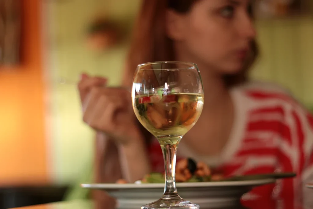 Un verre de vin posé devant une femme qui mange un plat