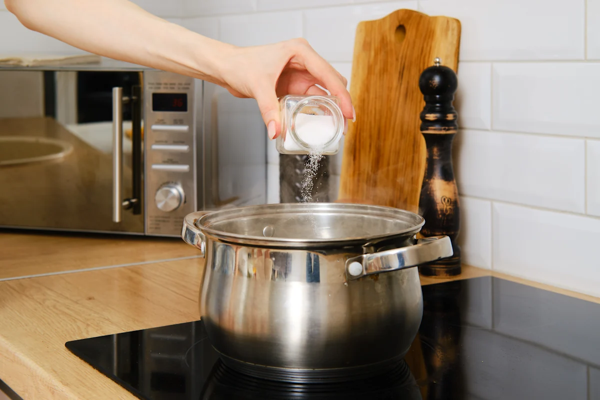 Une personne qui verse du sucre blanc dans une casserole à fond épais